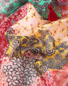 Close-up of the red patchwork scarf showing the pink, yellow and cream ditsy floral panels and a red tassel.