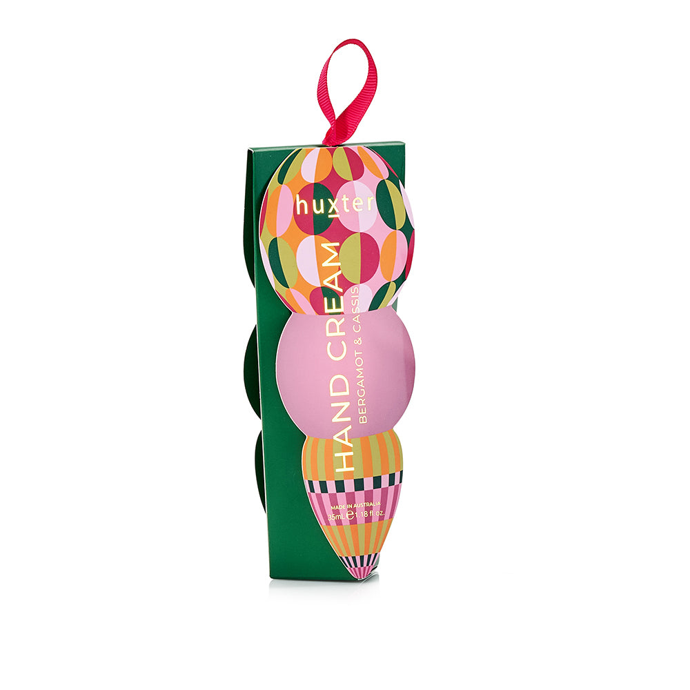 Green Huxter hand cream box with a circle-patterned bauble and a pink circle on the front, and a pink ribbon loop.
