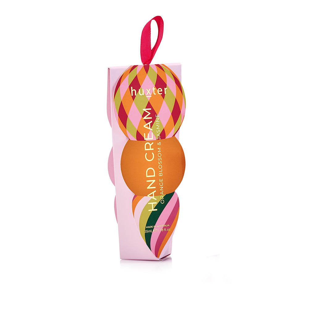 Pink Huxter hand cream box with a diamond-patterned bauble and an orange circle on the front, and a pink ribbon loop.
