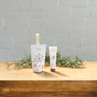 The Rose Geranium hanging hand cream box beside its 30 mL tube on a wooden table with pine sprigs.