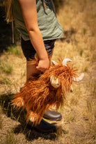 A child in a green T-shirt walking through dry grass, carrying the cow at their side.
