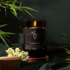 Lit Himalayan Bamboo candle glowing in its dark reclaimed wine bottle beside bamboo foliage