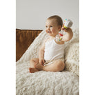 Baby sitting on a cream throw, shaking the maracas rattle up beside their shoulder.