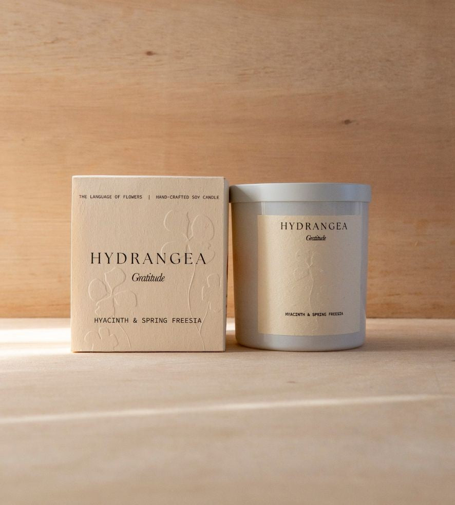 The Hydrangea candle in its white vessel beside its cream box.
