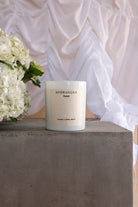 The Hydrangea candle on a concrete plinth with white hydrangeas and draped fabric behind.