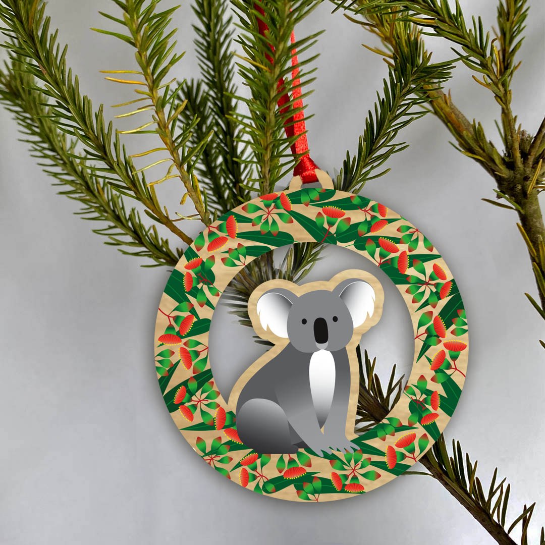 The Koala ornament hanging on a pine branch by its red loop.