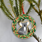 The Koala ornament hanging on a pine branch by its red loop.