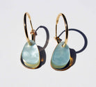 A pair of gold hoop earrings, each hung with a smooth organic teardrop of pale aqua marbled acrylic over a slim gold mirror panel.