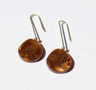 A pair of long gold hook earrings, each hung with a flat round disc of warm brown tortoiseshell marbled acrylic.