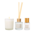 The three pieces in the set: a lit candle in a ribbed glass, a small reed diffuser with a gold collar and a small eau de parfum bottle with a gold cap