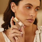 Woman holding the small eau de parfum bottle with a gold cap to her cheek