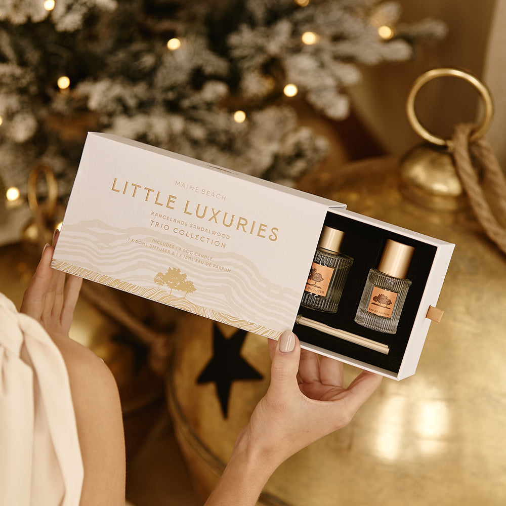 Hands sliding the Rangelands Sandalwood Little Luxuries box open to show the bottles inside, with Christmas decorations behind