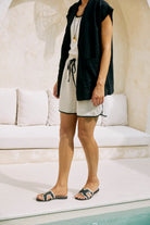 Model by a pool in a black vest and linen shorts, wearing the black Maris slides