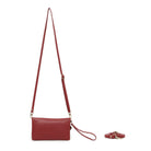 The red wallet hanging from its long cross body strap, wrist strap attached, with a third strap coiled beside it.