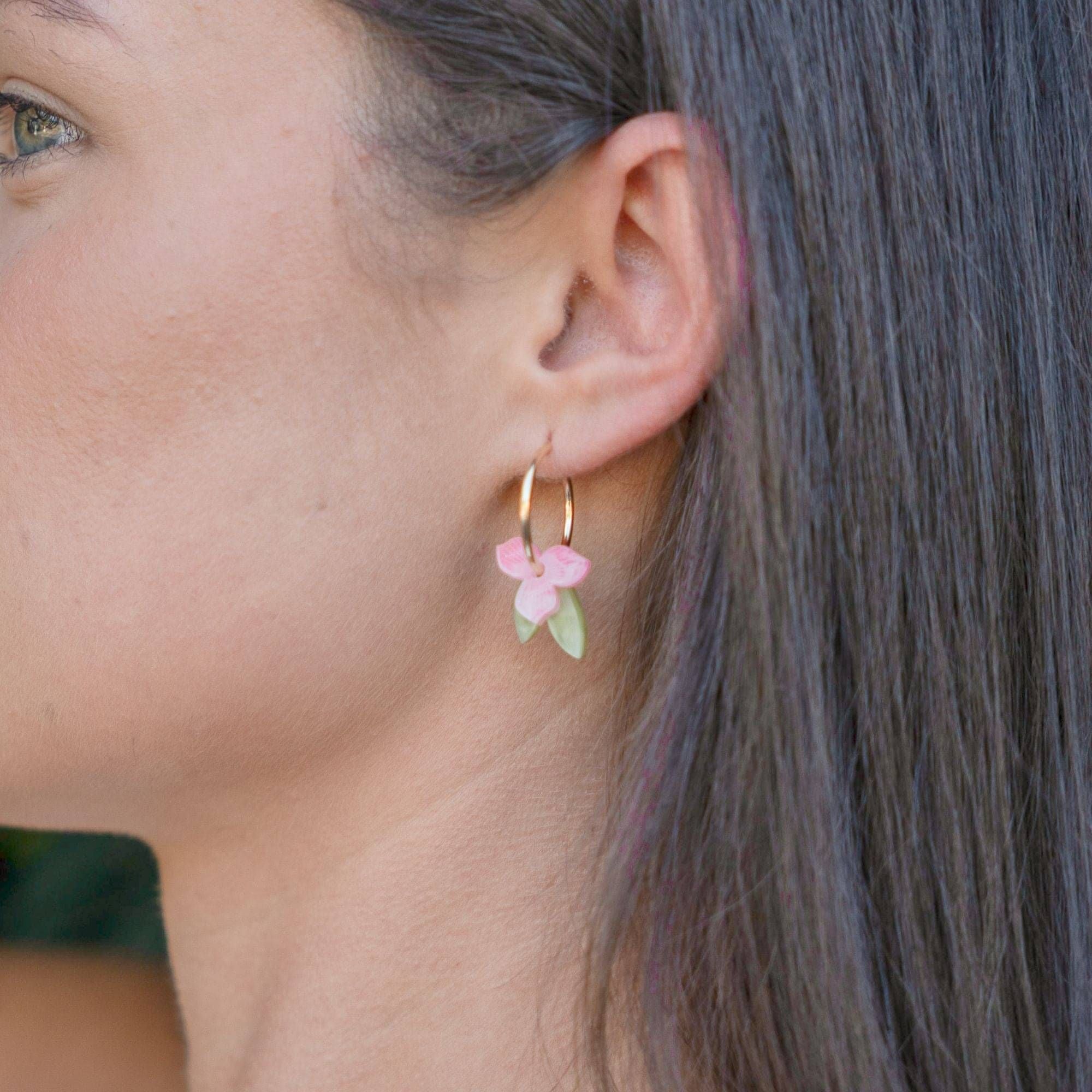 A close-up of a person wearing the soft pink flower and green leaf hoop earring, seen from the side with hair swept back.