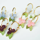 Four pairs of gold hoop earrings laid together, each hung with a small marbled acrylic flower and green leaf, in pale blue, white, deep burgundy and soft pink.