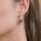 A close-up of a person wearing the deep burgundy flower and green leaf hoop earring, seen from the side with hair swept back.
