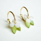 A pair of gold hoop earrings, each hung with a small white flower and a slender green leaf in marbled acrylic.
