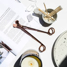 Rose gold wick trimmer beside a lit Mojo candle and open magazine