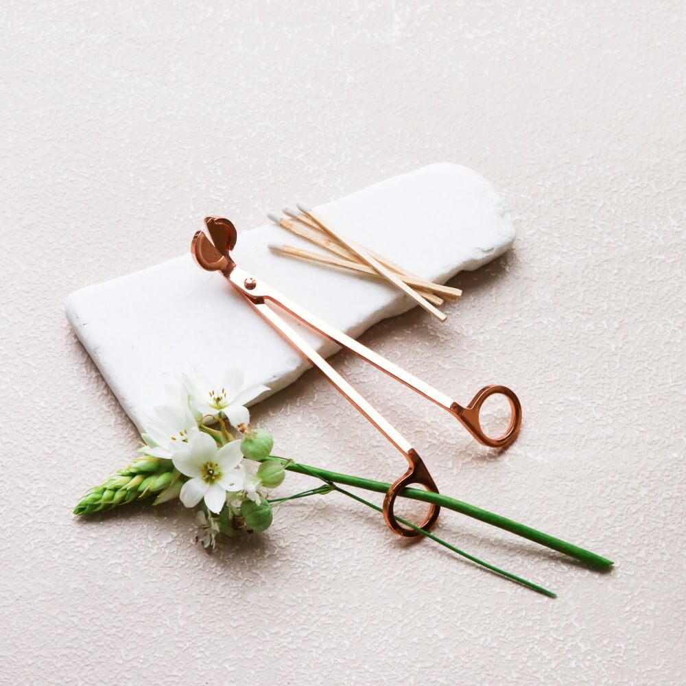 Rose gold wick trimmer on white stone with fresh white flowers