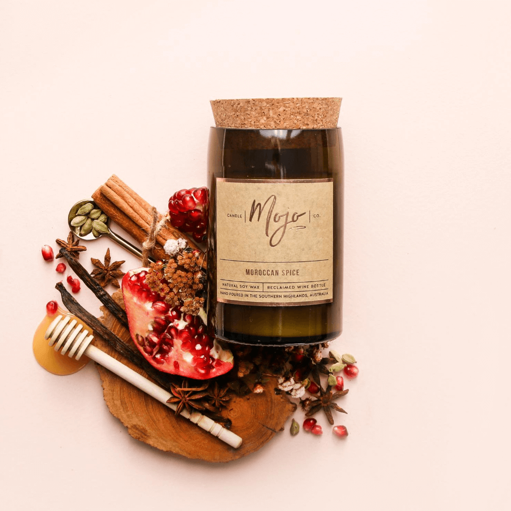 Moroccan Spice candle on blush with a honey dipper, pomegranate half, star anise and pink peppercorns