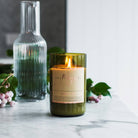 Lit Watermelon Lemonade candle on marble beside a ribbed glass carafe and berries