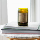 Lit Cedar & Saffron candle on a stack of magazines on a marble side table by a bright window