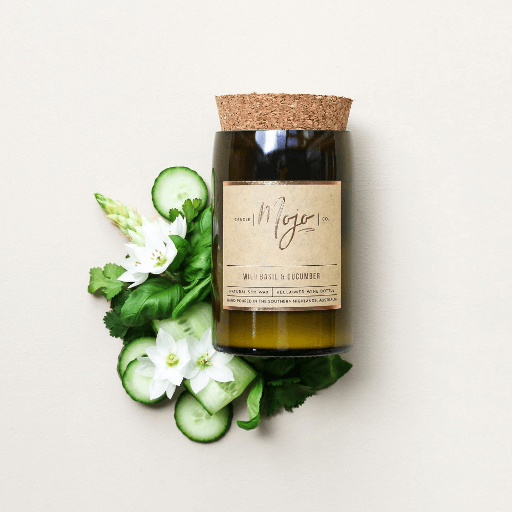 Wild Basil & Cucumber soy candle in a cork-topped reclaimed wine bottle with cucumber slices and white flowers