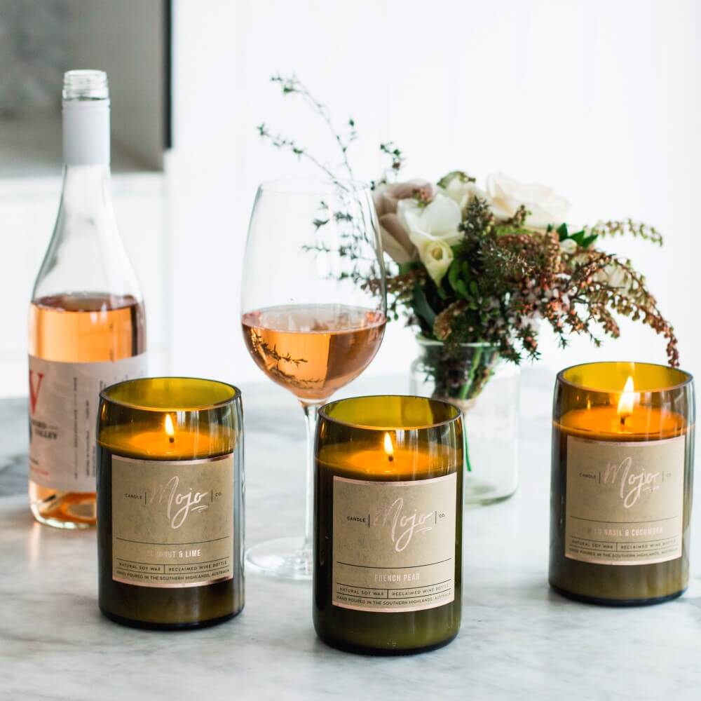 Three lit Mojo reclaimed wine bottle candles on marble with rose wine and flowers