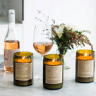 Three lit Mojo reclaimed wine bottle candles on marble with rose wine and flowers