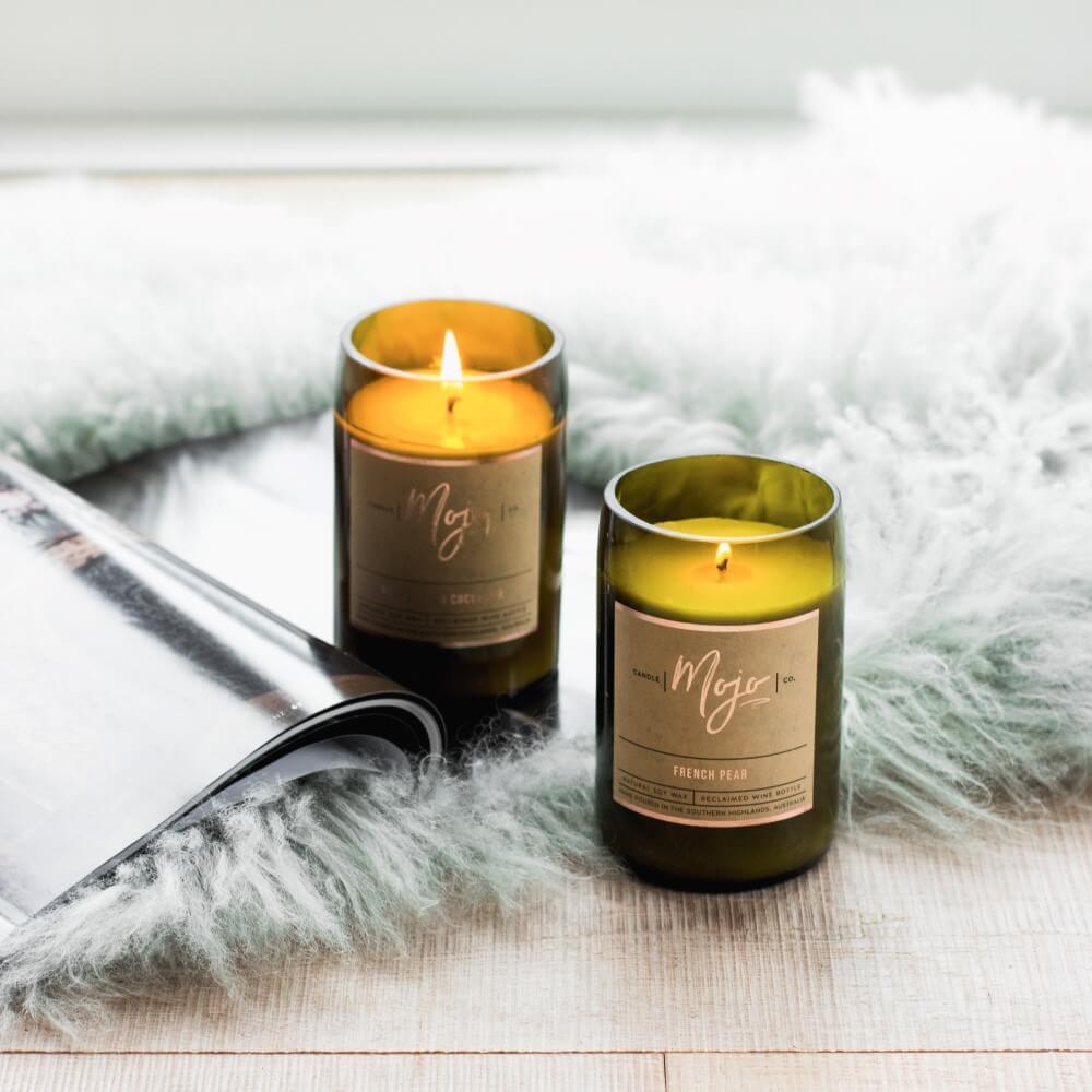 Two lit Mojo reclaimed-bottle candles resting on a sheepskin throw with a magazine