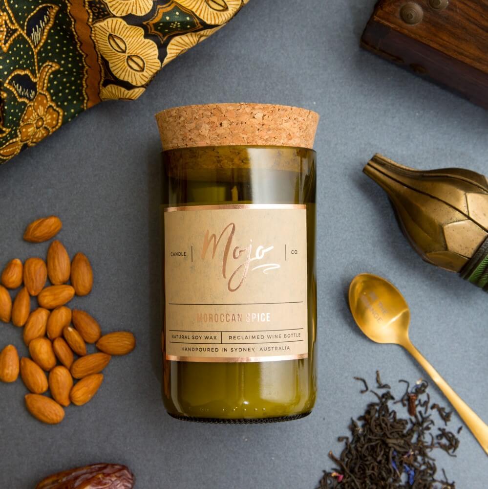 Moroccan Spice candle on grey with gold-patterned fabric, almonds, dates, a gold spoon and loose tea