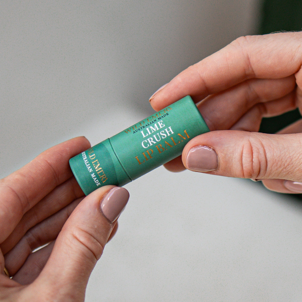 Hands holding the green Key Lime Crush lip balm tube.
