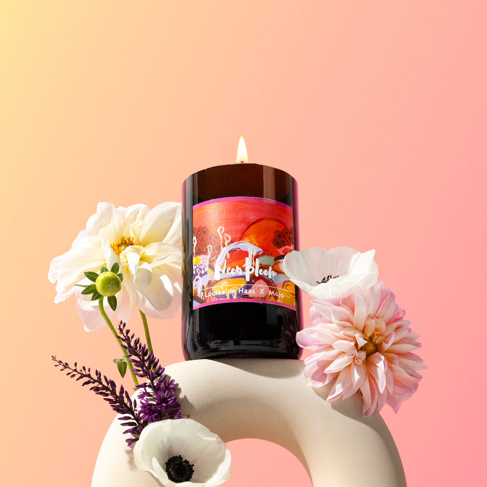 Lit Neon Bloom candle with dahlias in a sculptural vase on a peach backdrop