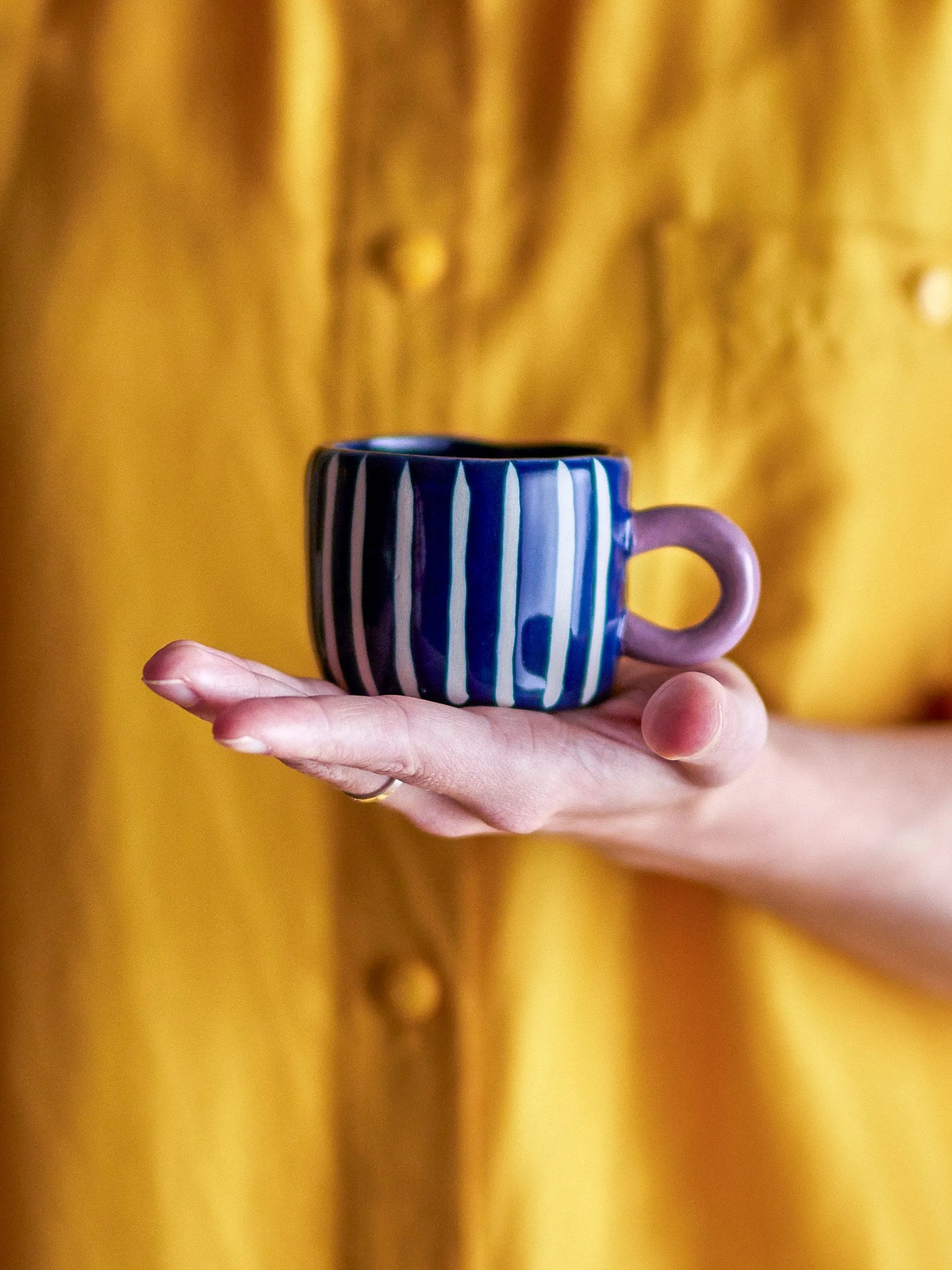 The blue-stripe Nini cup held on an open hand, its lilac handle to the side.
