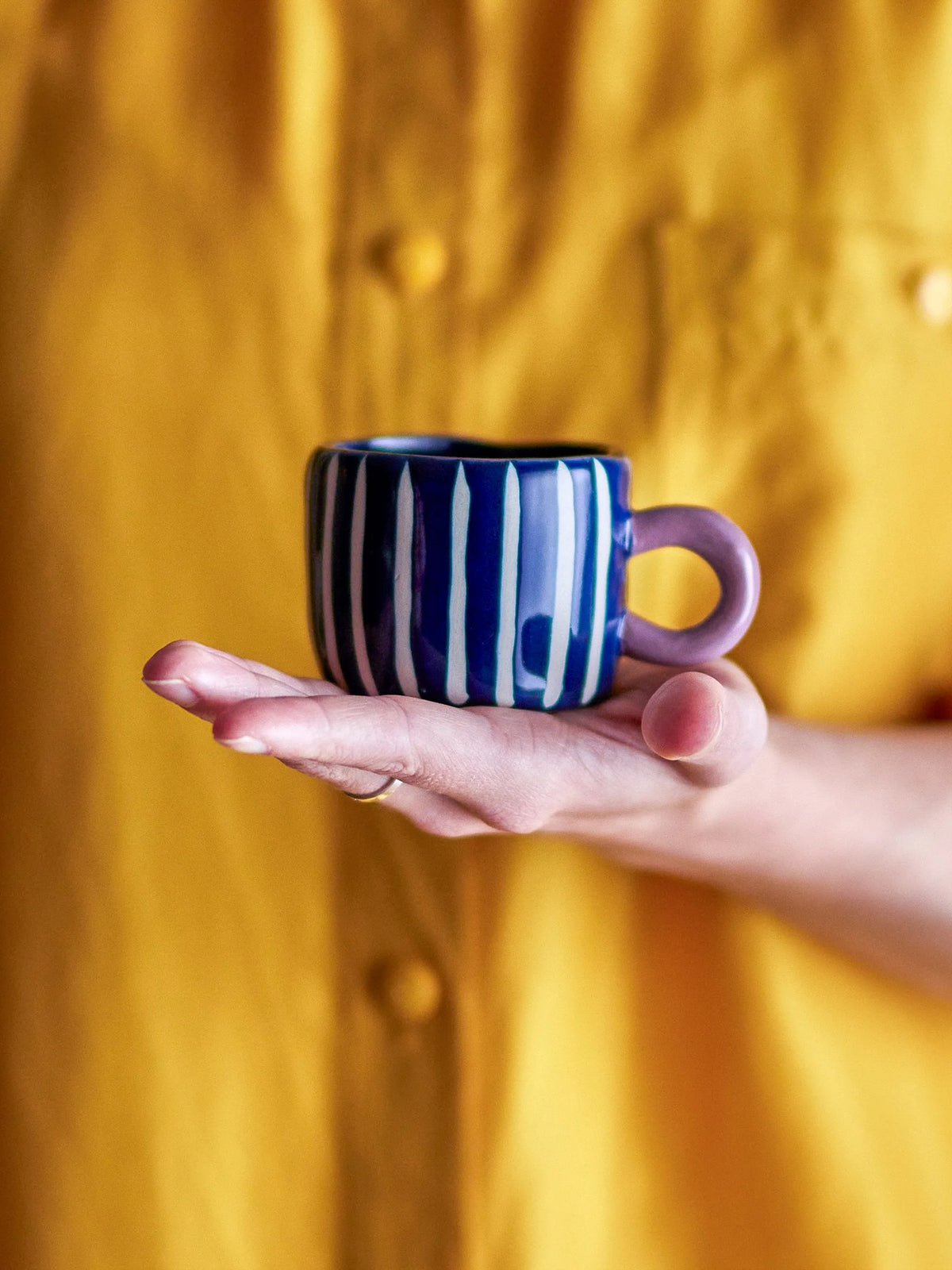 The blue-stripe Nini cup held on an open hand, its lilac handle to the side.