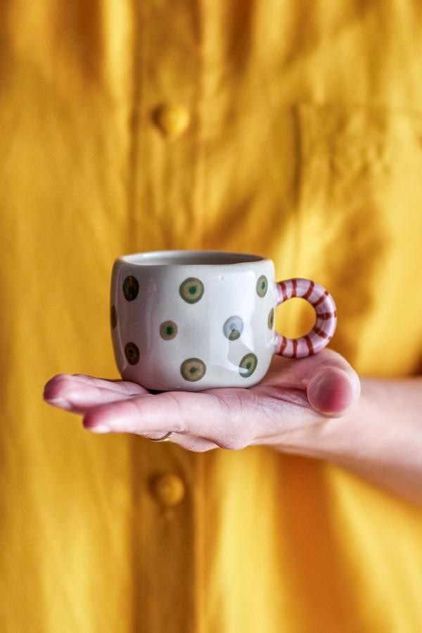 The green-dot Nini cup held on an open hand, its striped handle to the side.