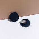 A pair of matte black acrylic disc clip-on earrings, one turned over to show the clip.