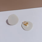 A pair of ivory beige acrylic disc clip-on earrings, one turned over to show the clip.