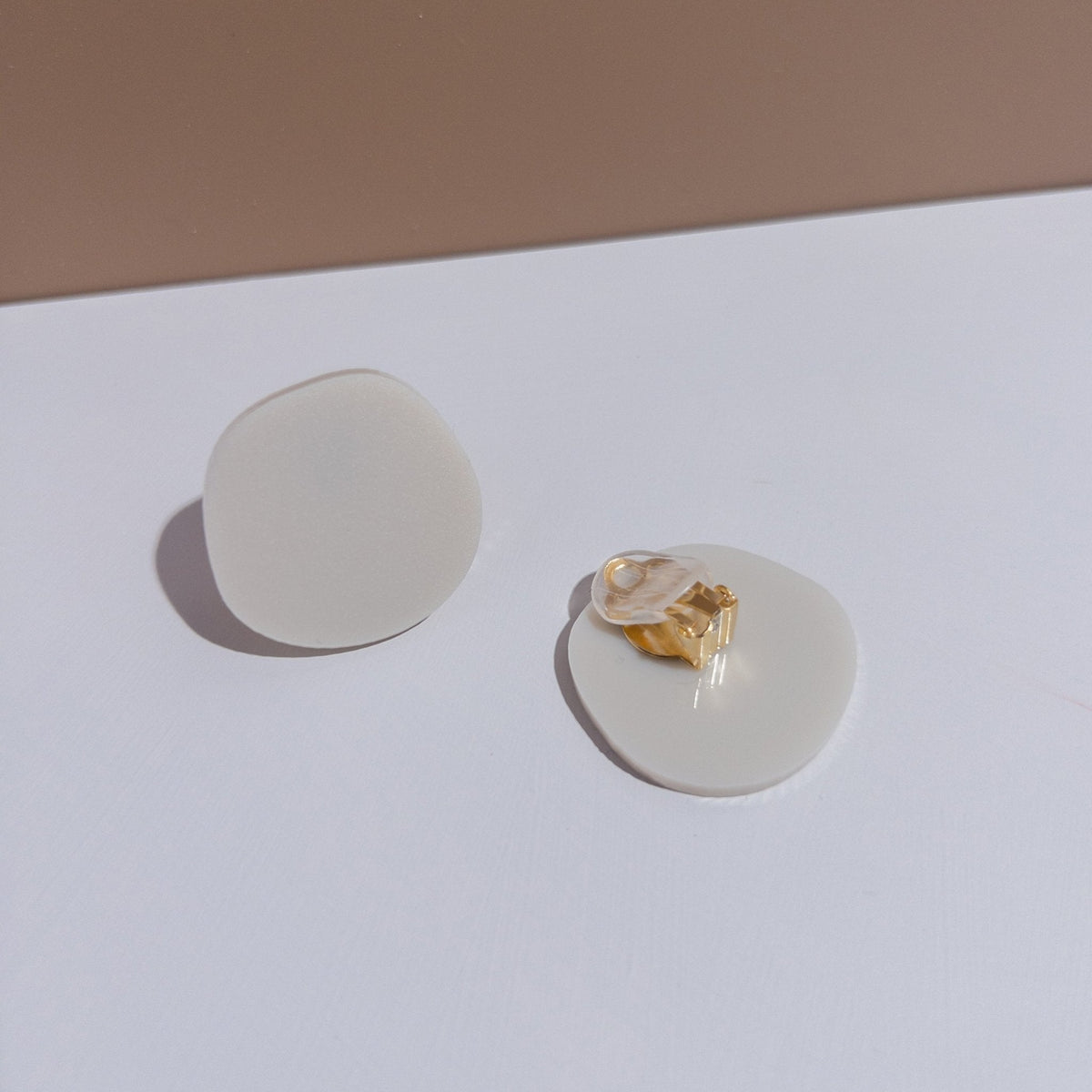 A pair of ivory beige acrylic disc clip-on earrings, one turned over to show the clip.
