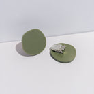 A pair of olive green acrylic disc clip-on earrings, one turned over to show the clip.