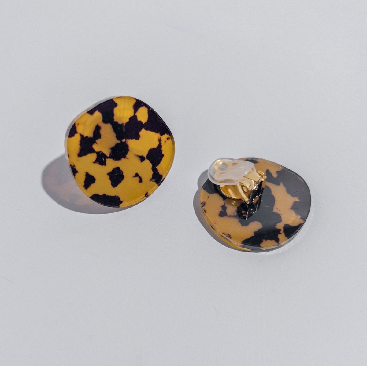 A pair of honey and black tortoiseshell acrylic disc clip-on earrings, one turned over to show the clip.