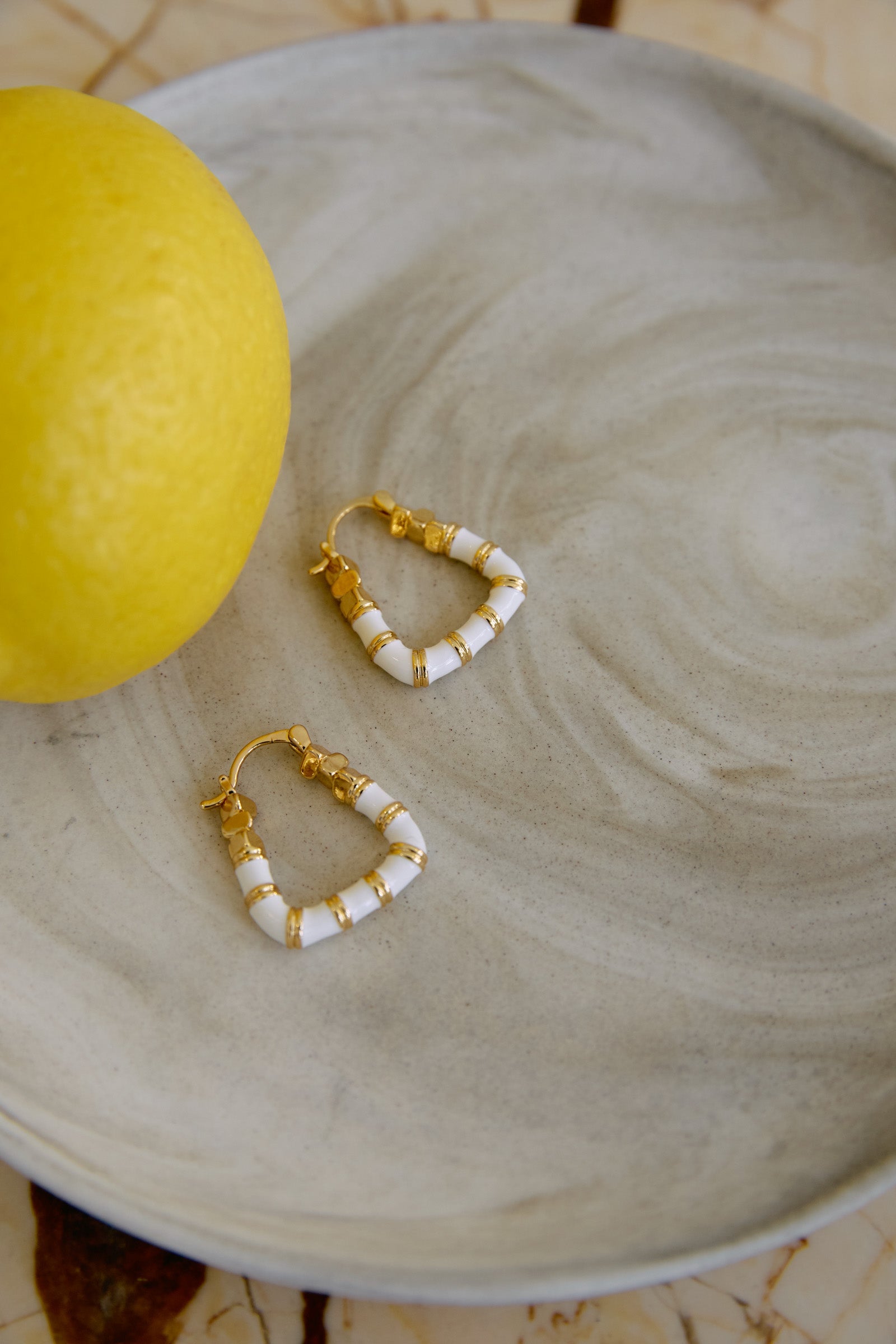 A pair of White Parisio hoops on a pale marbled plate beside a lemon