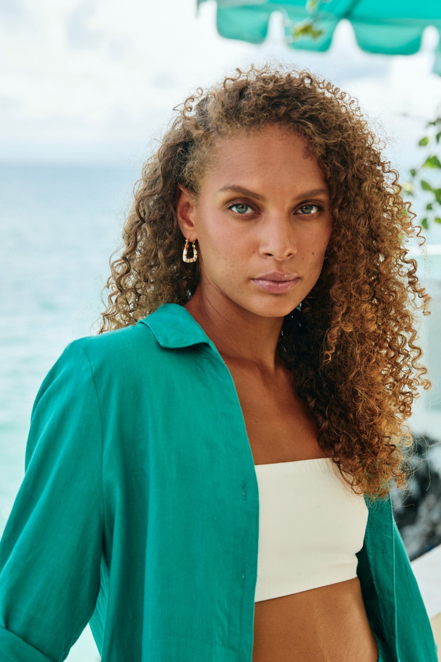 Model in a green shirt by the sea wearing a White Parisio hoop