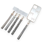 Five crystal-set phone wrist straps with clear attachment tabs, beside a phone case with a bow print