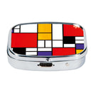 Silver-tone metal pill box with a Mondrian-style grid of red, yellow, blue and black blocks set in the lid.