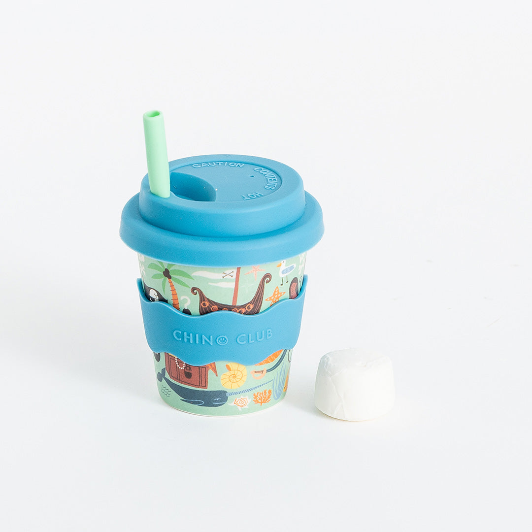 Pirate babychino cup: pirate ships, a treasure chest and sea creatures on mint, with a blue lid and wavy sleeve, a green straw and a marshmallow beside it