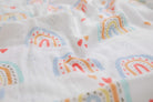 Close-up of the print: soft rainbows in blue, orange and red with tiny hearts on white muslin.