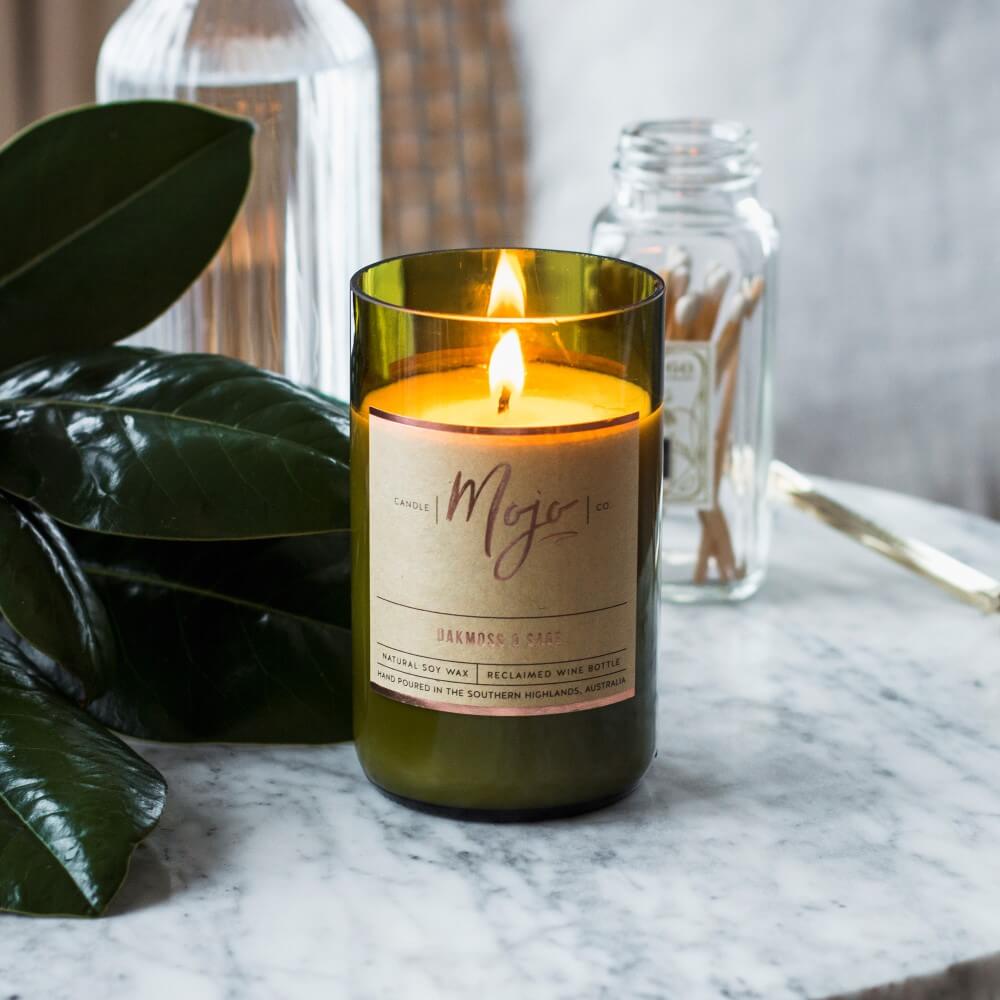 Lit Wild Basil & Cucumber candle on a marble table with magnolia leaves