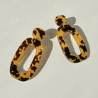 A pair of honey and dark brown tortoiseshell acrylic dangle earrings, each an open oval hung from a small rounded top.